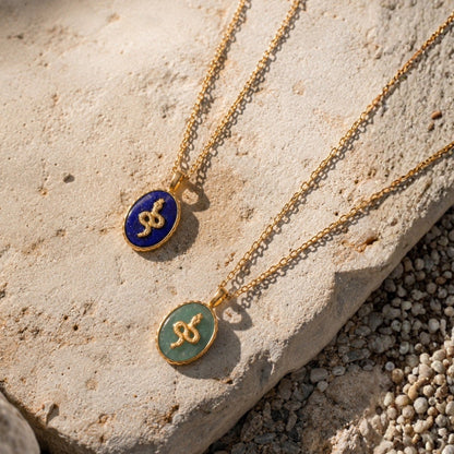 Two gold necklaces with blue and green pendants on a stone surface