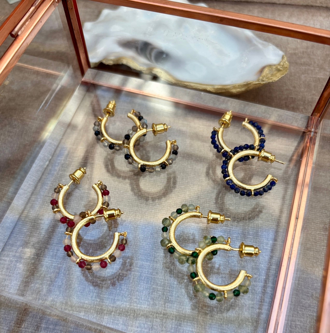 Gold hoop earrings with gemstones on a reflective surface