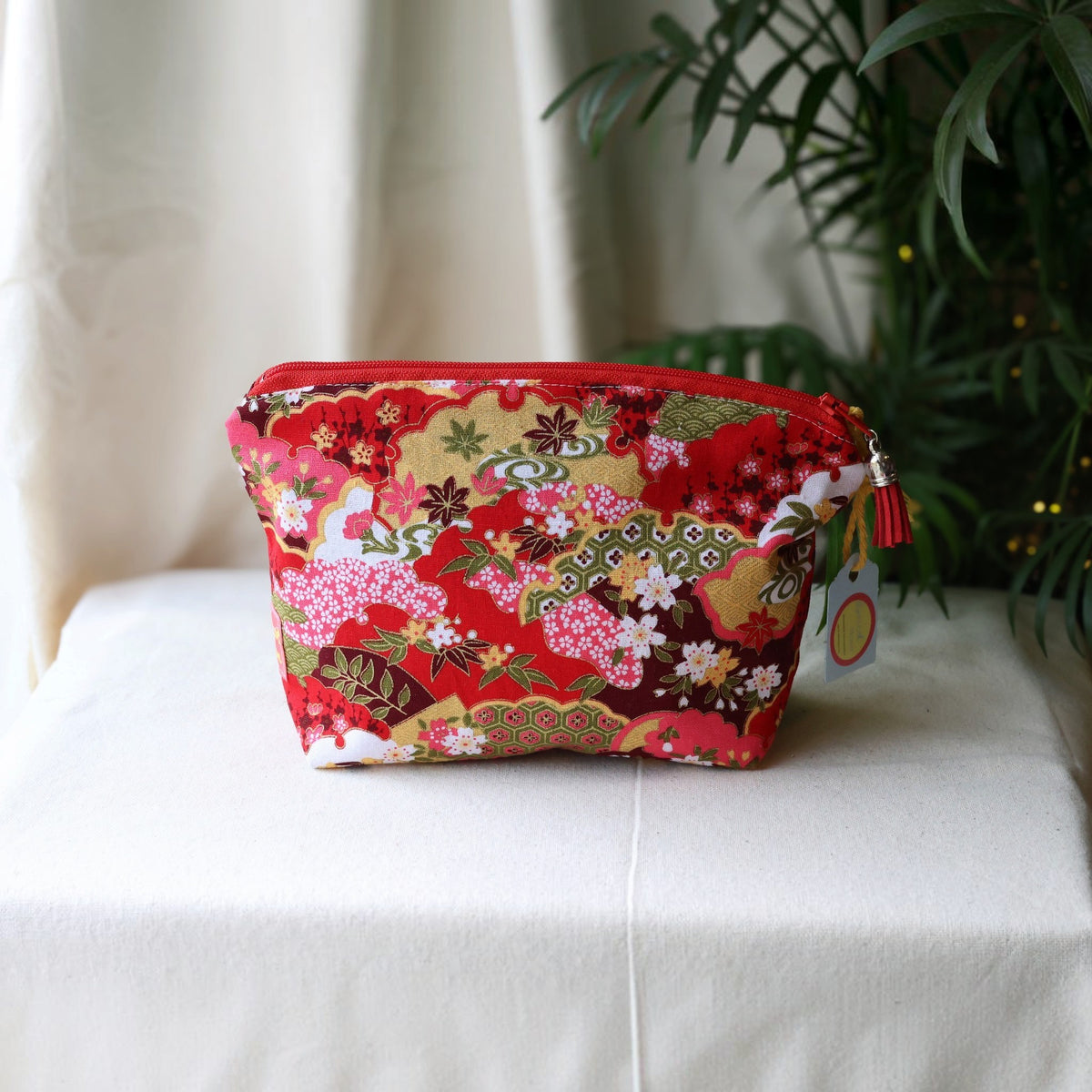 Isumi Red Japanese everyday pouch with a red zip and red tassel on a cream cloth beside a palm plant