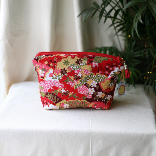 Isumi Red Japanese everyday pouch with a red zip and red tassel on a cream cloth beside a palm plant