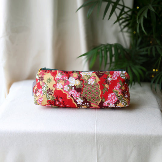 Isumi Red Japanese pencil case with a dark green zip on a cream cloth beside a palm plant