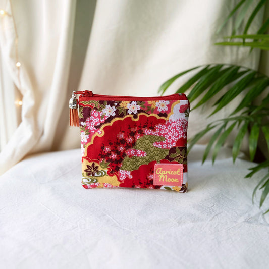 Isumi Red Japanese purse with a red zip and orange tassel on a cream cloth beside a palm plant