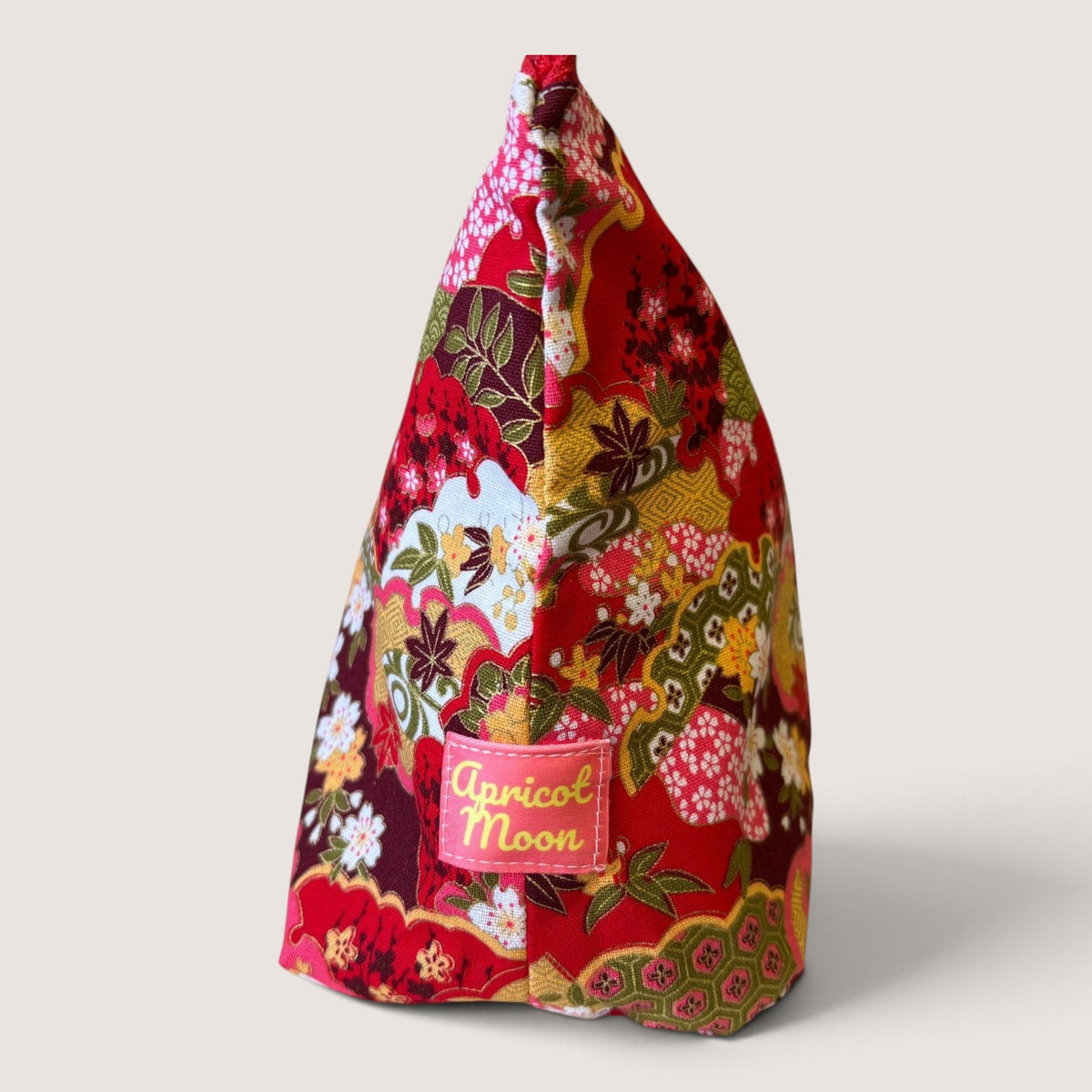 Isumi Red Japanese wash bag with a red zip and pink suede tassel, angled view