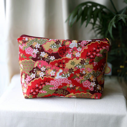 Isumi Red Japanese wash bag with a burgundy zip on a cream cloth beside a palm plant