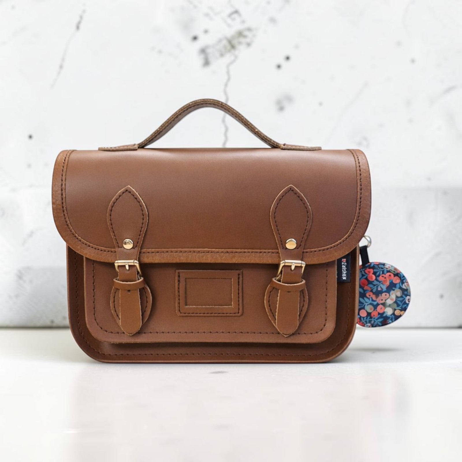 Brown leather satchel with floral tag on a white background