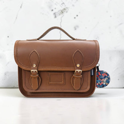 Brown leather satchel with floral tag on a white background