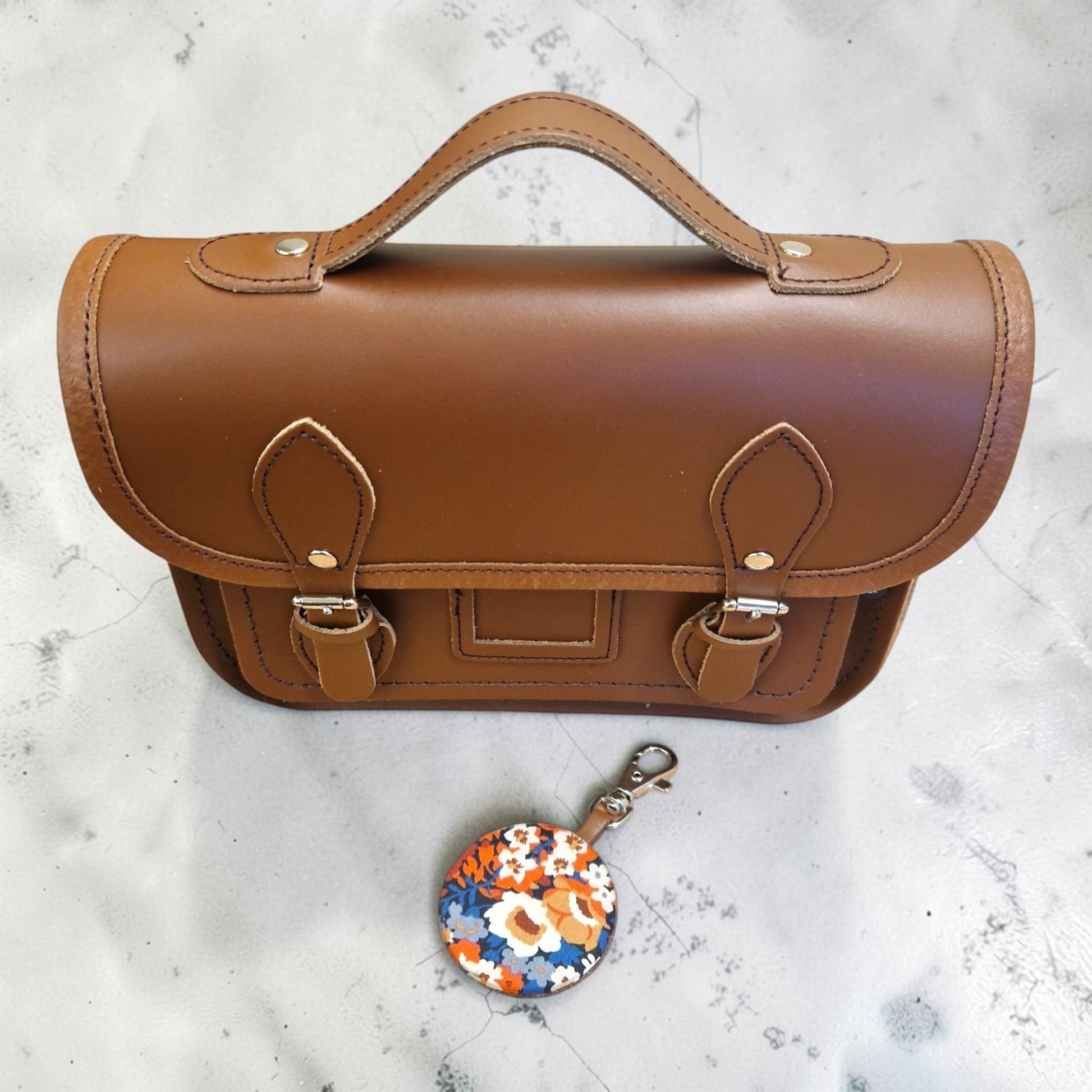 Brown leather satchel with a floral keychain on a light gray surface