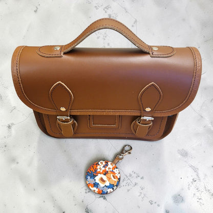 Brown leather satchel with a floral keychain on a light gray surface