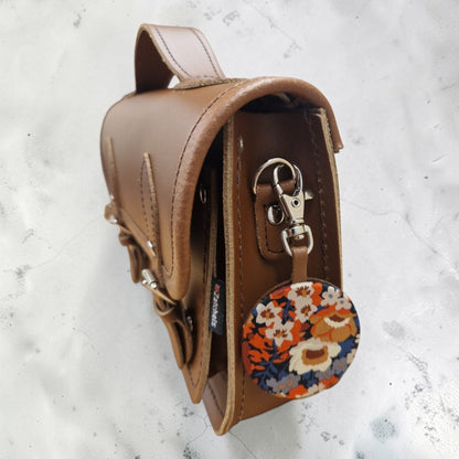 Brown leather bag with floral keychain on a light gray background