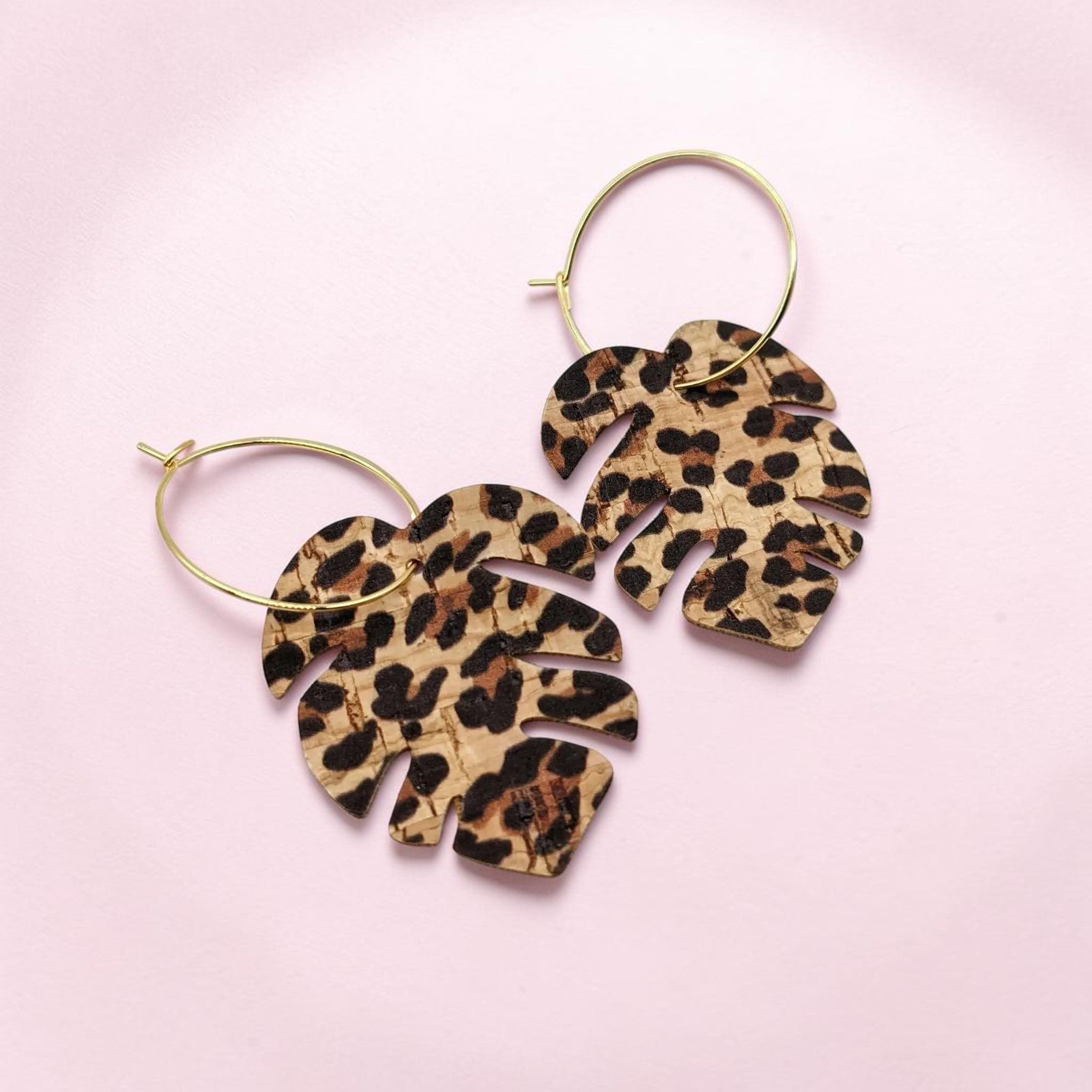 Leopard print leaf-shaped earrings on a pink background