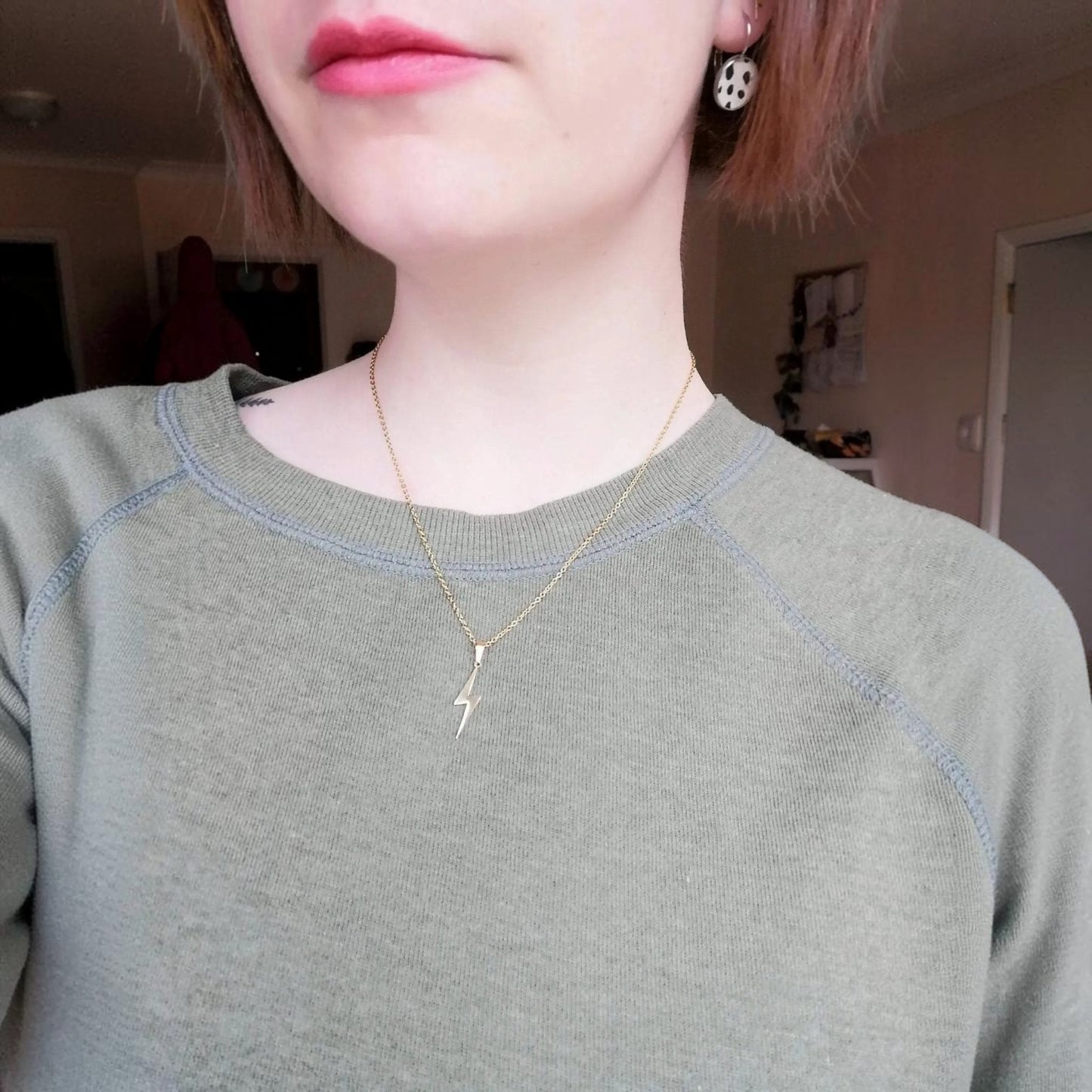 Person wearing a gold necklace with a small pendant indoors.