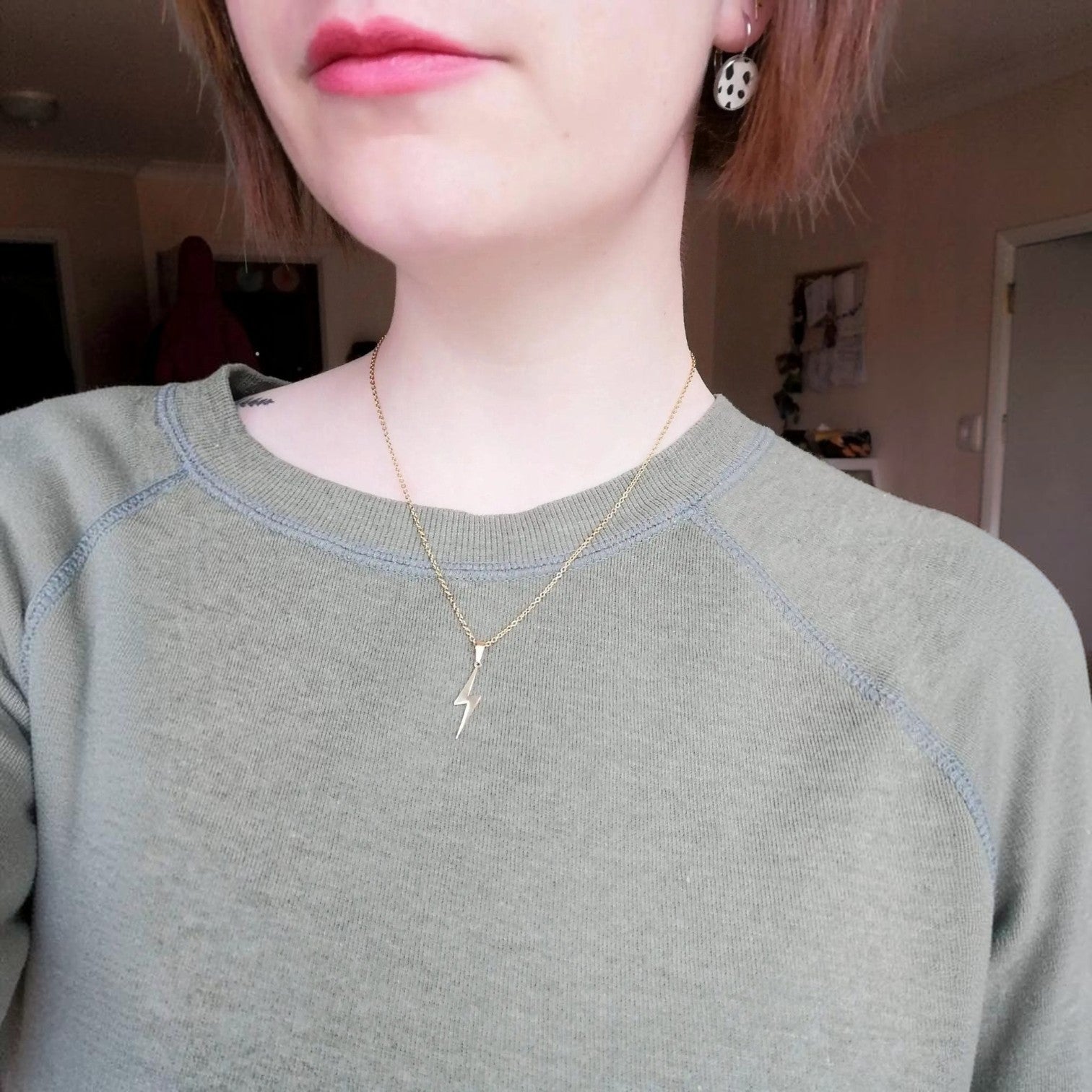 Person wearing a gold necklace with a small pendant indoors.