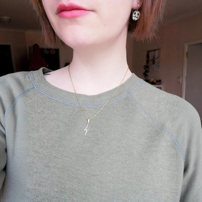 Person wearing a gold necklace with a small pendant indoors.