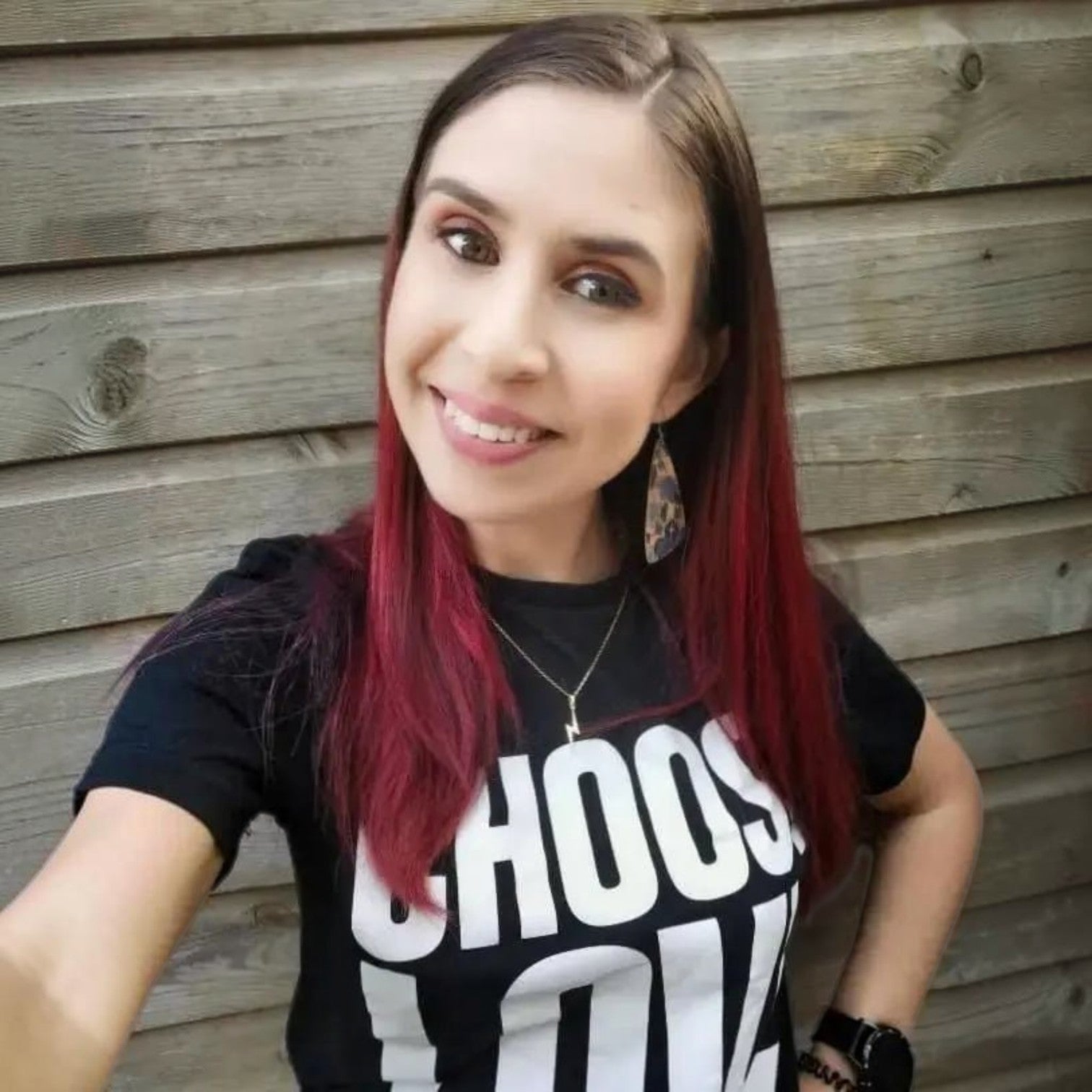 Woman with red hair wearing a black t-shirt with white text against a wooden background