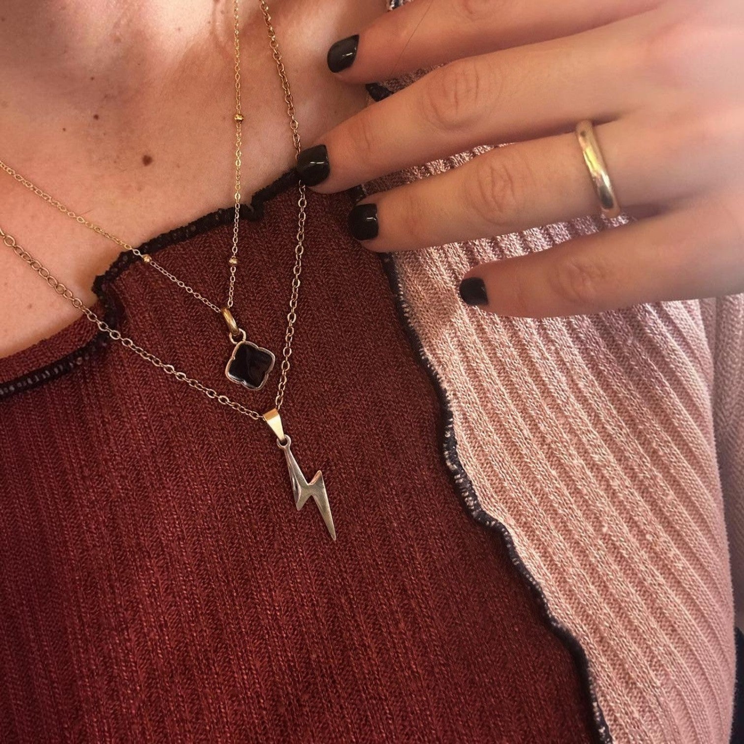 Close-up of a hand wearing multiple necklaces with a lightning bolt pendant on a textured surface.