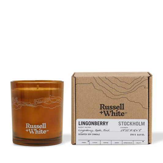 Brown candle with 'Russell + White' branding next to its packaging on a white background