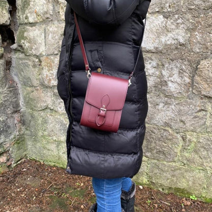 Person wearing a black puffer coat with a red handbag against a stone wall.