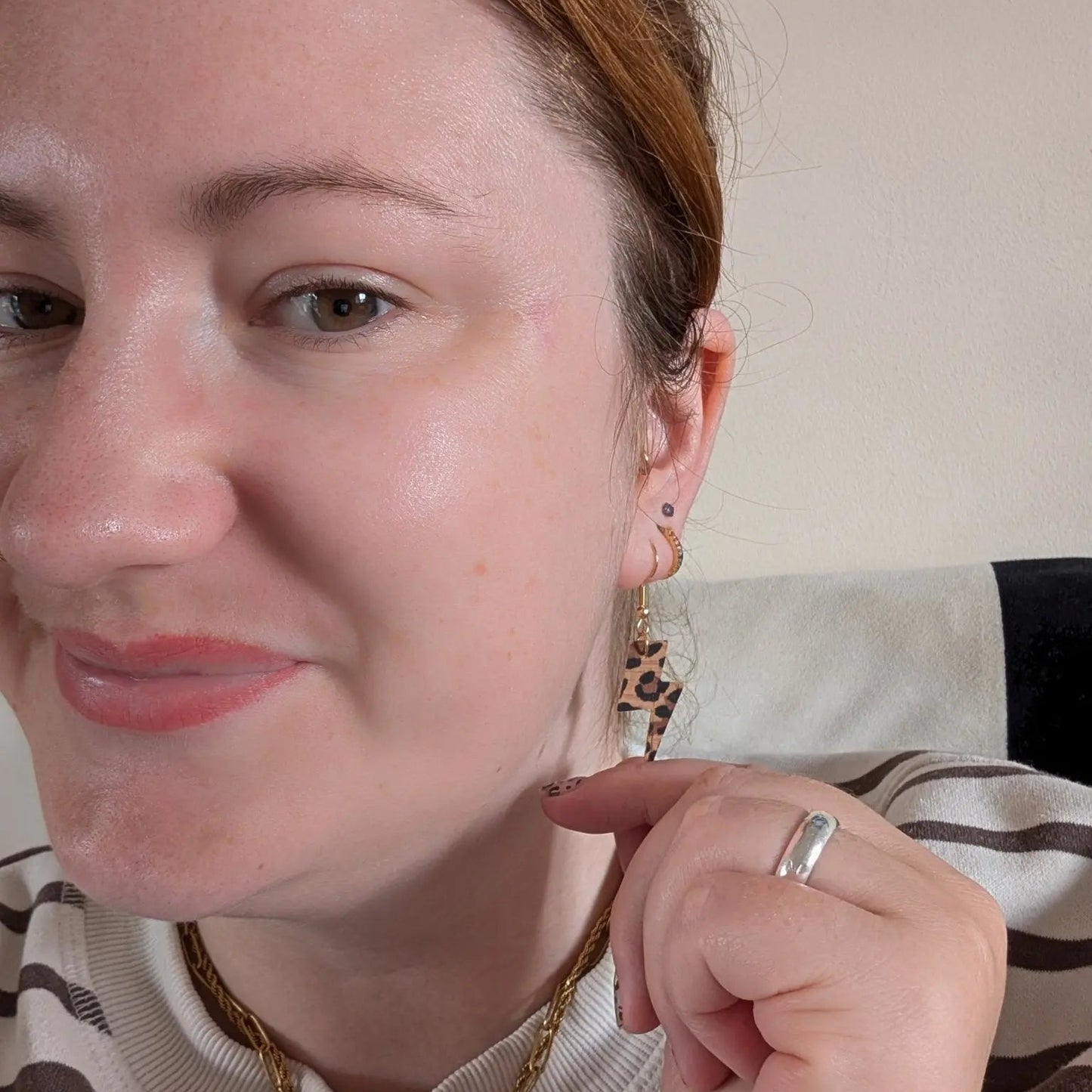 Close-up of a woman wearing gold earrings and a ring, with a neutral background.