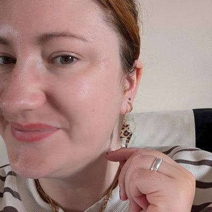 Close-up of a woman wearing gold earrings and a ring, with a neutral background.