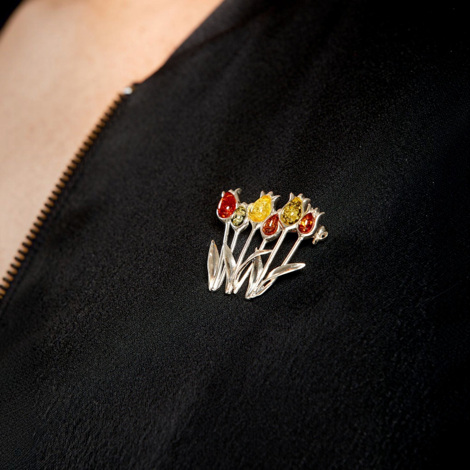 A silver-tone floral brooch with red, yellow, and orange flower details, pinned to a black velvet jacket worn by a model.