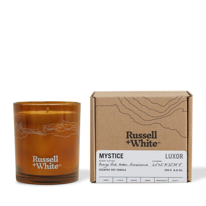 Brown candle with 'Russell + White' branding next to its packaging on a white background