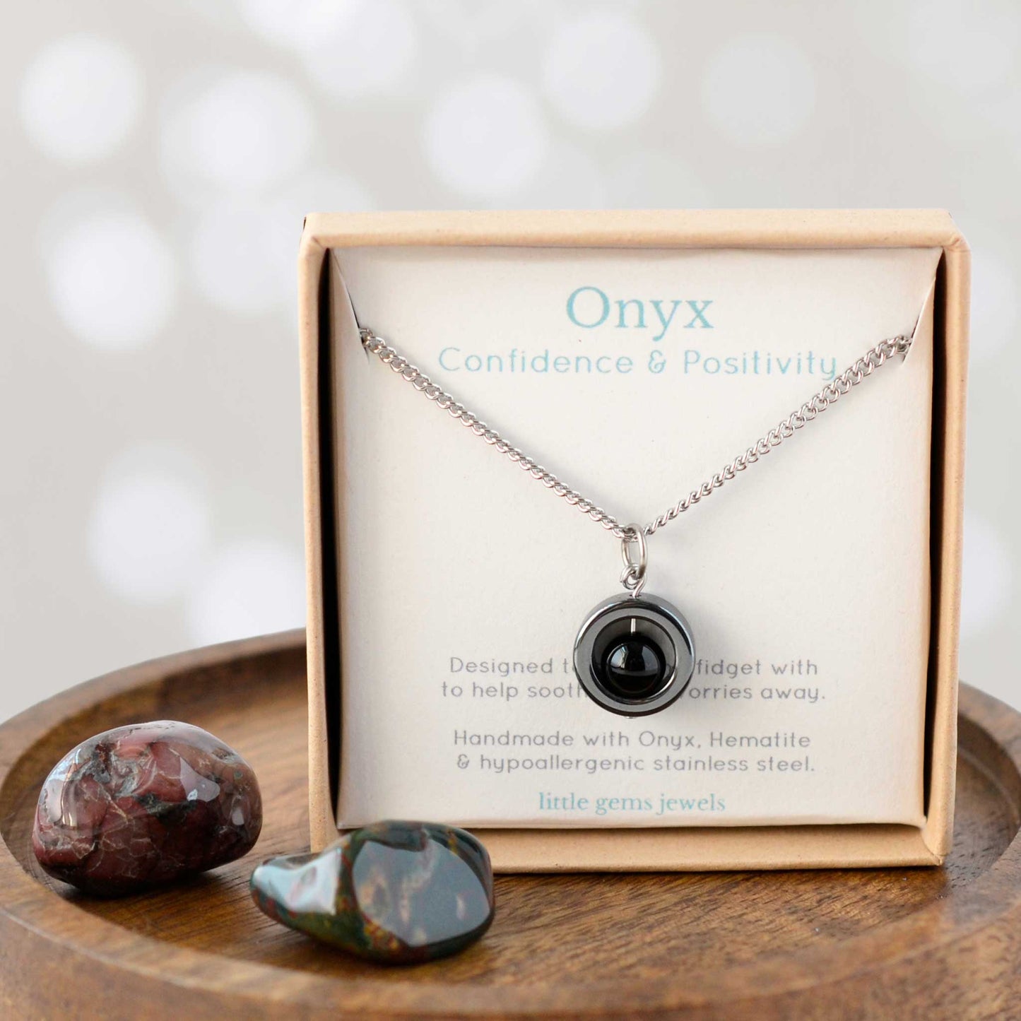 Onyx necklace in a wooden box with a card explaining its properties, on a wooden surface.
