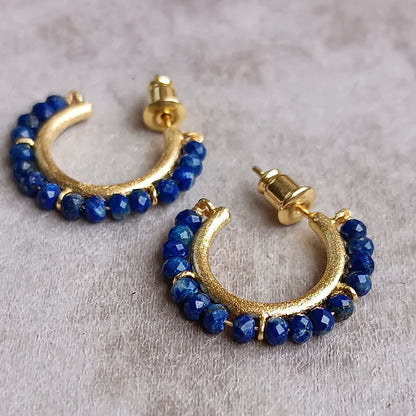 Gold hoop earrings with blue beads on a light gray background