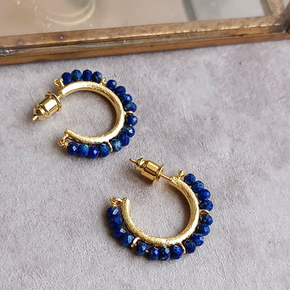 Gold hoop earrings with blue beads on a light gray surface.