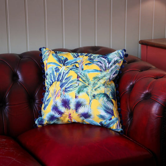 Palm Springs velvet cushion with navy pompoms on a deep red leather Chesterfield sofa