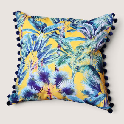 Palm Springs velvet cushion with navy pompoms, front view studio shot showing the yellow tropical palm and banana leaf print in teal, blue and purple, handmade in Dorset by Apricot Moon
