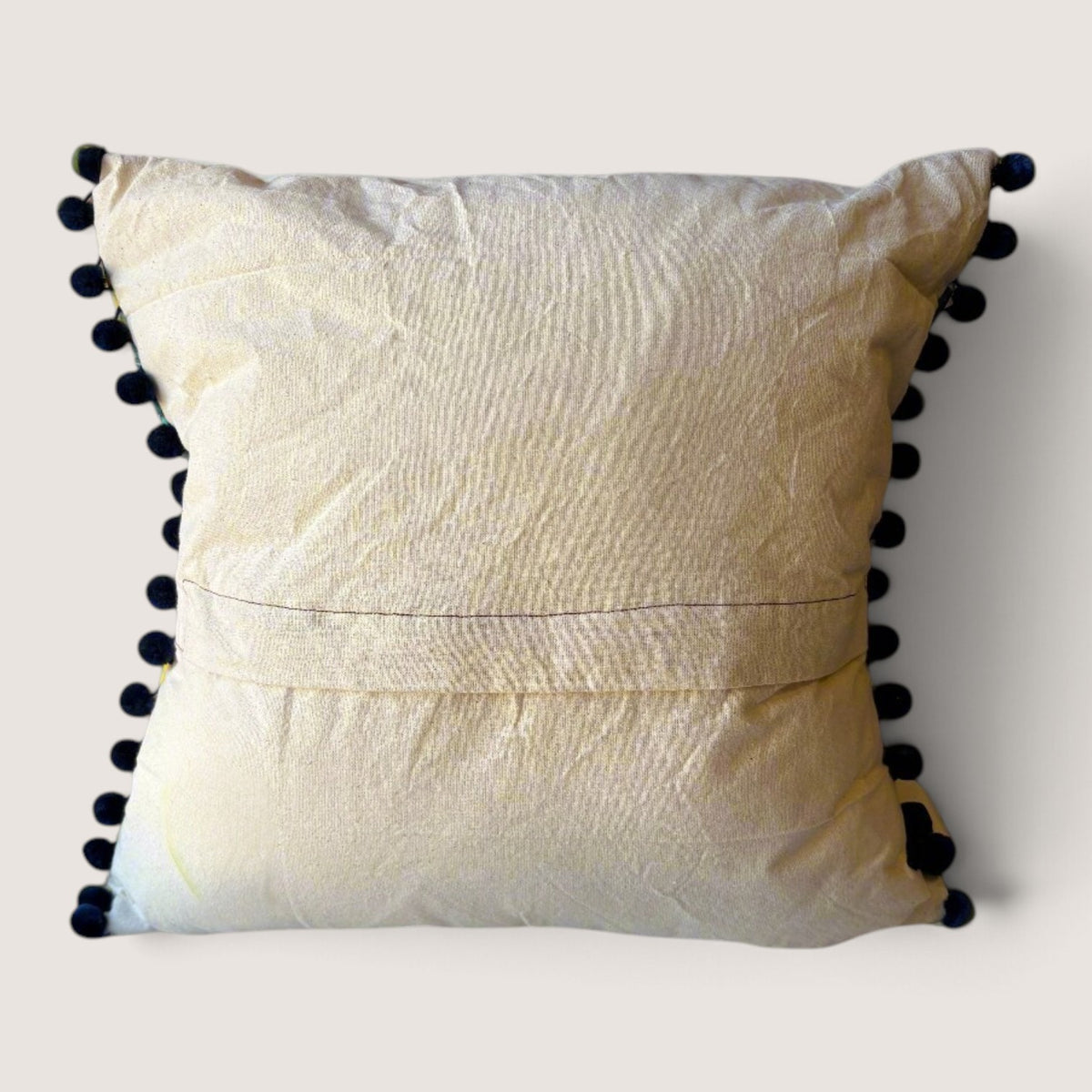 Rear view of the Palm Springs cushion with navy pompoms showing the plain cream back with an envelope opening