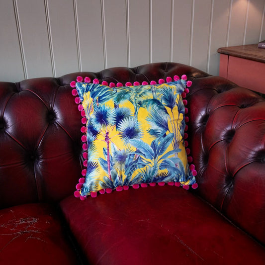 Palm Springs velvet cushion with strawberry pink pompoms on a deep red leather Chesterfield sofa