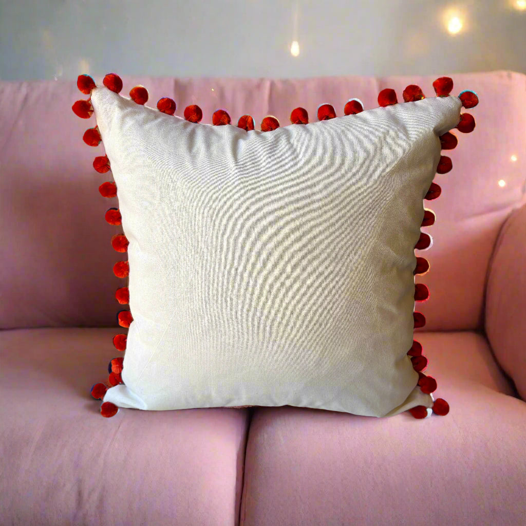 Rear view of the Palm Springs cushion showing the plain cream back with pompoms, on a pink sofa with fairy lights