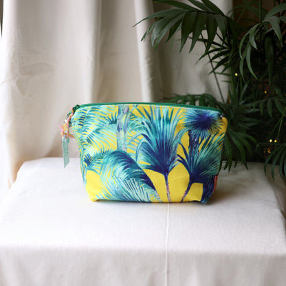 Palm Springs velvet everyday pouch with a green zip on a cream cloth beside a palm plant