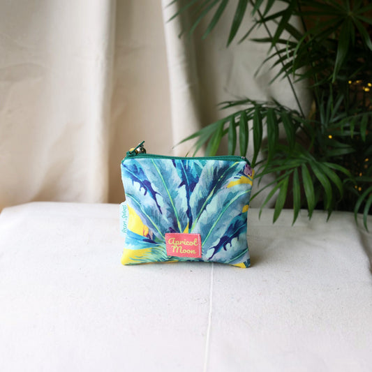 Palm Springs velvet purse with a green zip on a cream cloth beside a palm plant