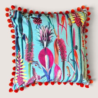 Paradise Blue velvet cushion with orange pompoms, front view studio shot showing the tropical botanical print in turquoise, pink, yellow and teal, handmade in Dorset by Apricot Moon