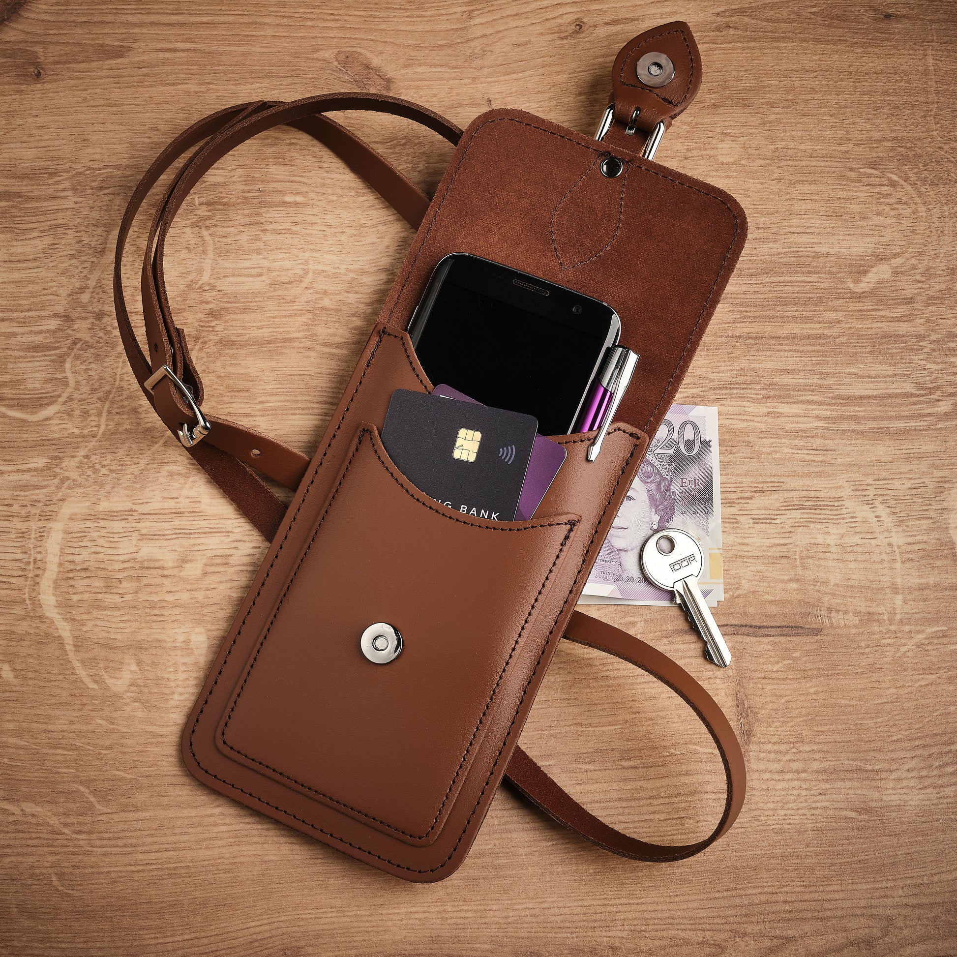 Brown leather crossbody bag with phone pocket on a wooden surface