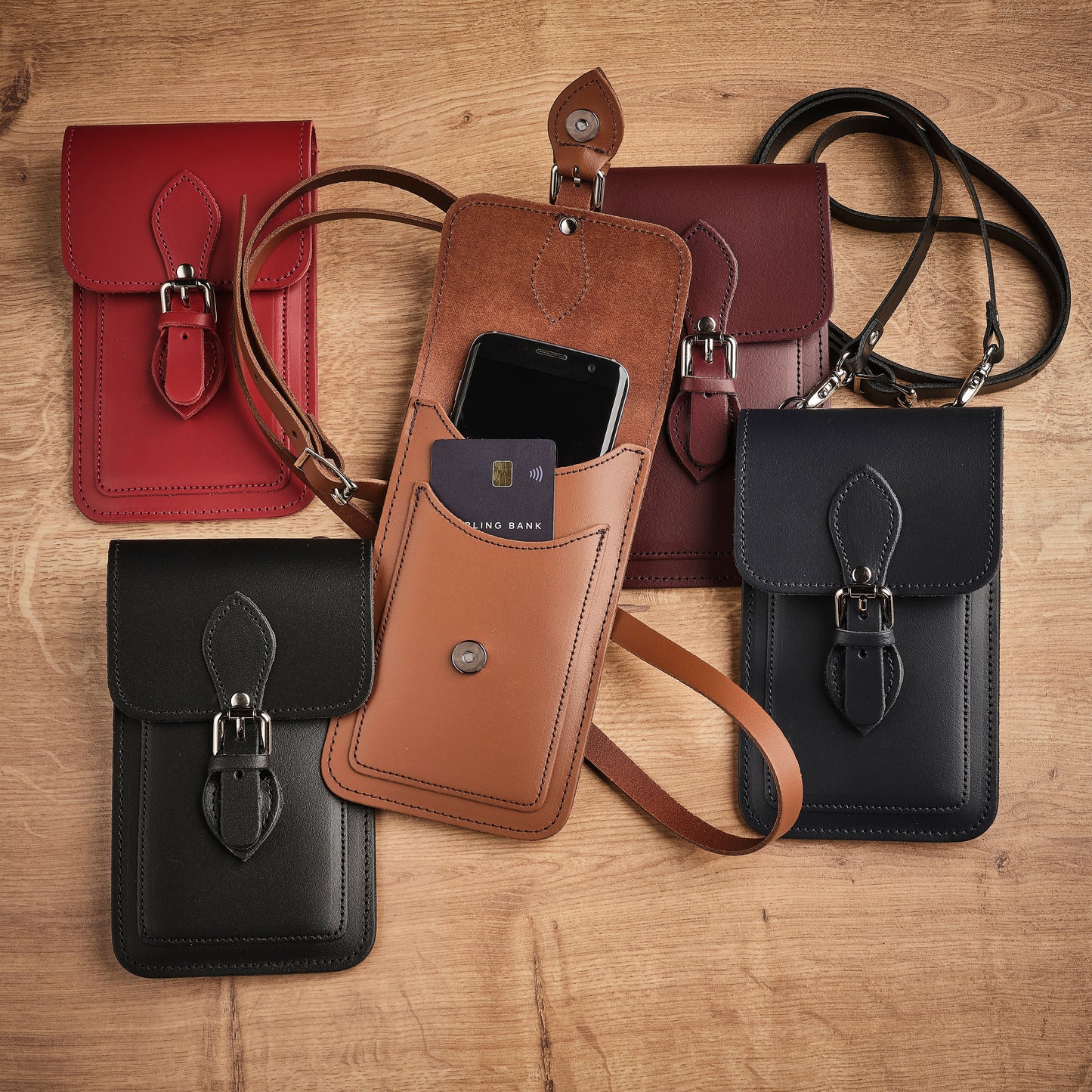 Collection of leather phone pouches in red, brown, and black on a wooden surface.