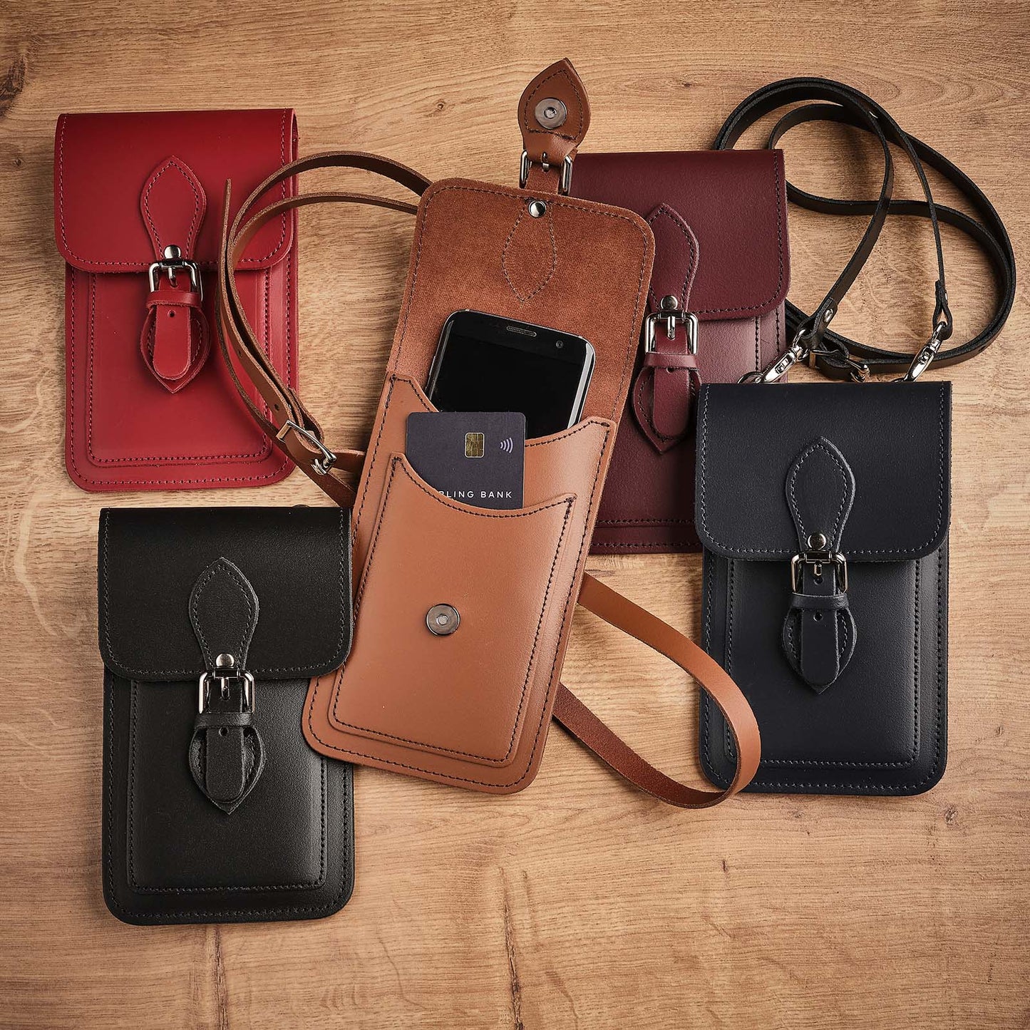 Collection of leather phone pouches in various colors on a wooden surface