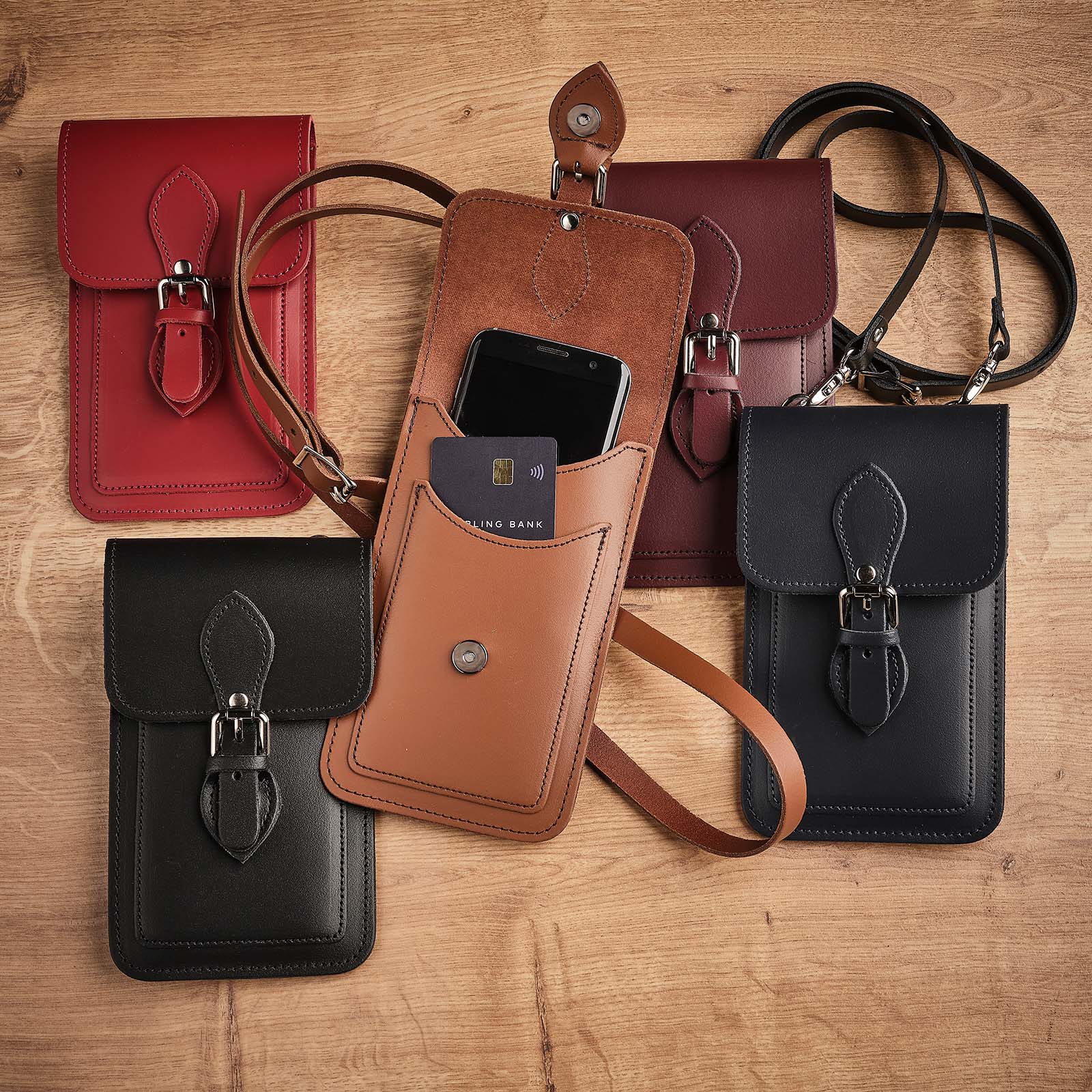 Collection of leather phone pouches in various colors on a wooden surface