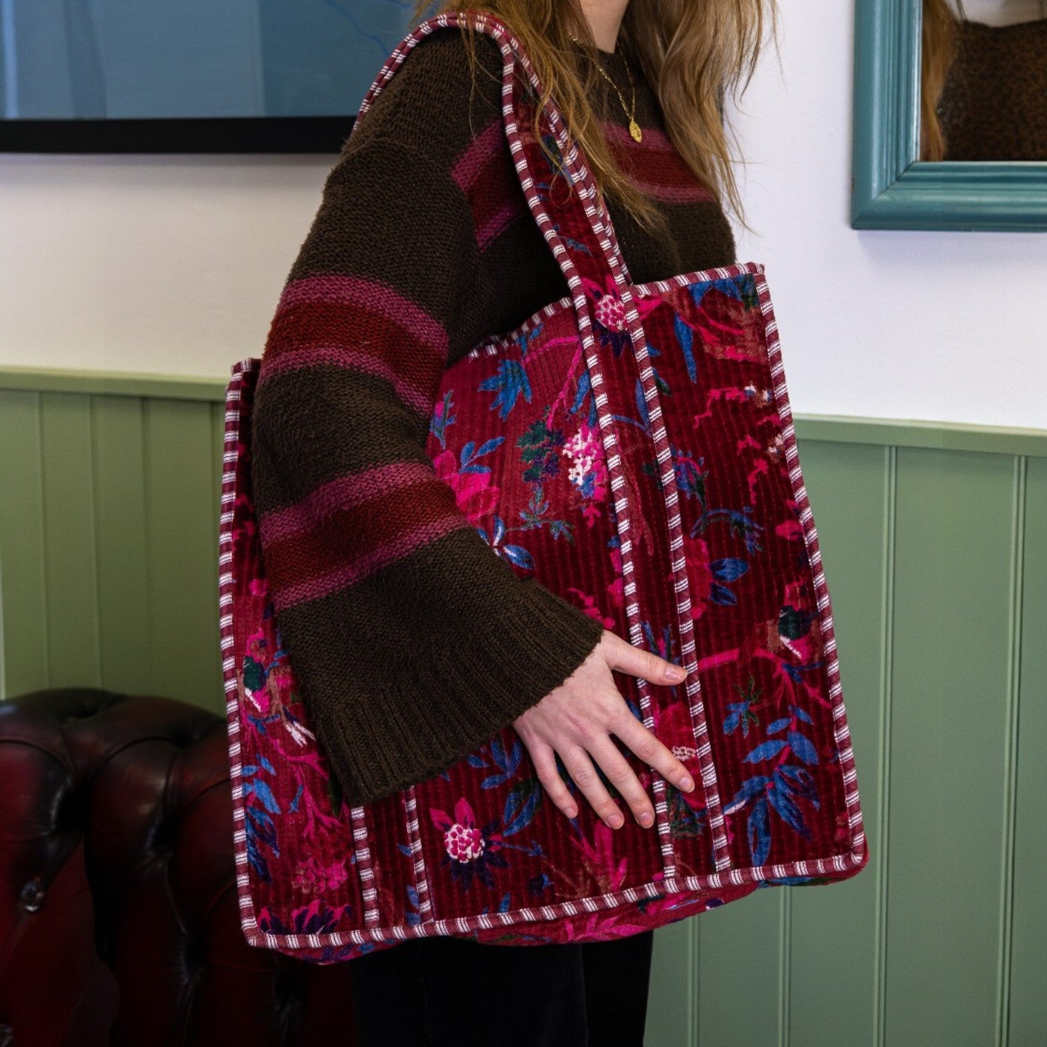 Person holding a vibrant, patterned bag with a green panel in the background