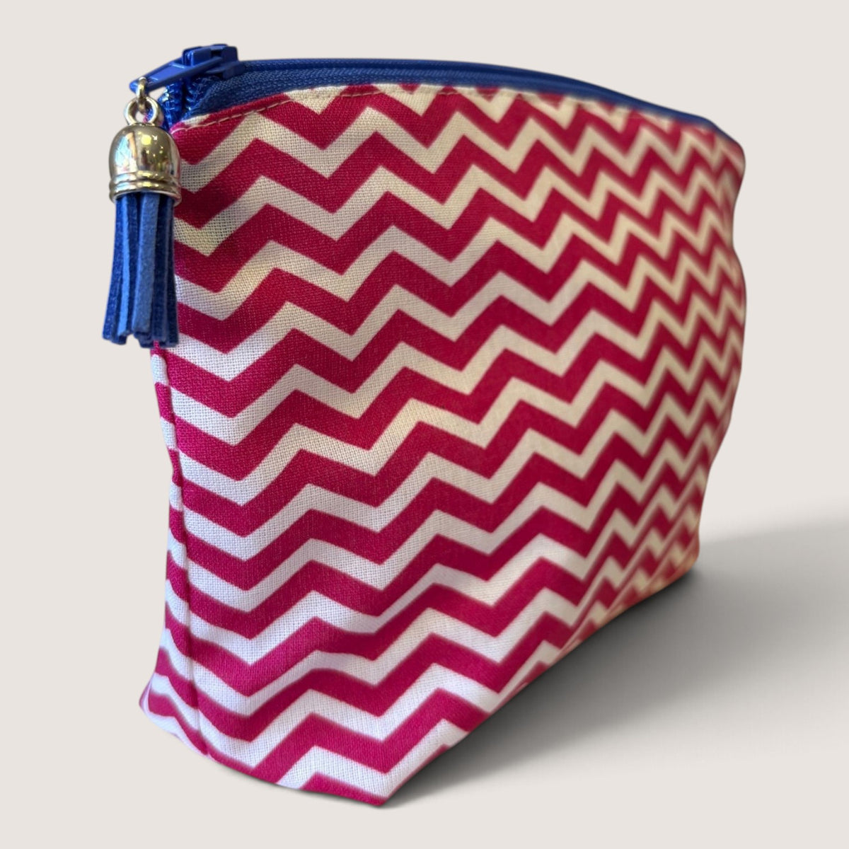 Raspberry Chevron everyday pouch angled to show the pink and white chevron print, navy blue zip and navy blue suede tassel with a silver cap