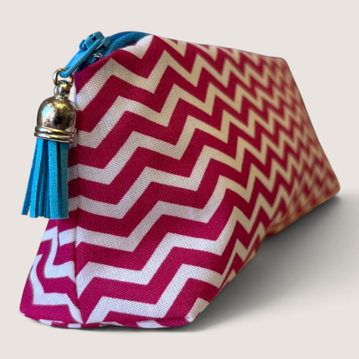 Raspberry Chevron pencil case angled to show the pink and white chevron print, bright blue zip and blue suede tassel with a silver cap