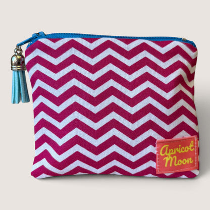 Front of the Raspberry Chevron coin purse in a raspberry pink and white zigzag print, with a bright blue zip, pale blue tassel and Apricot Moon label