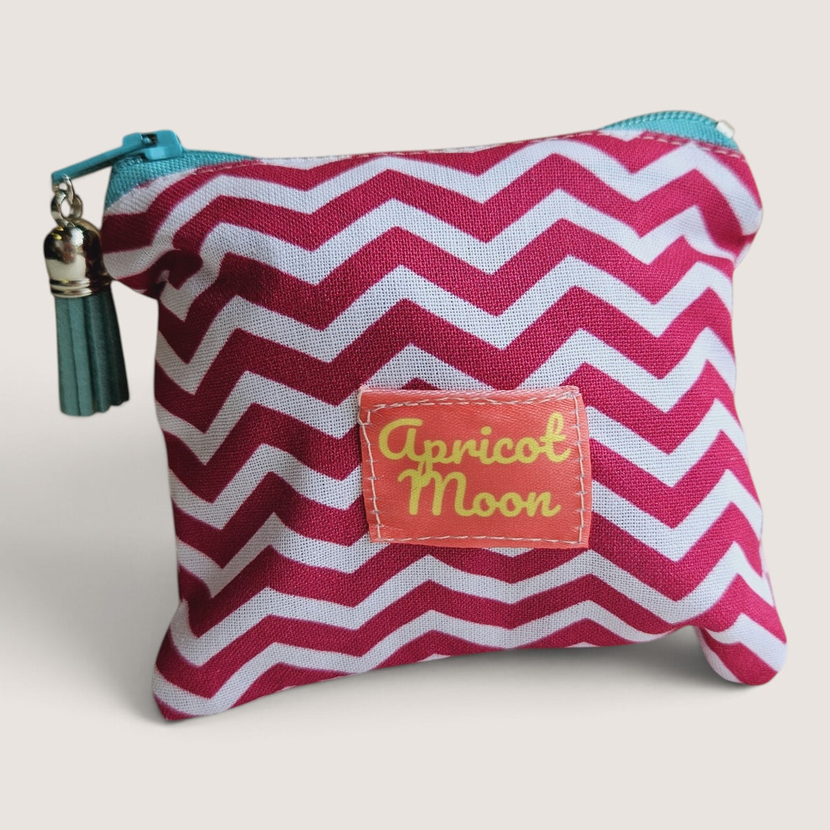 Raspberry Chevron coin purse in a pink and white chevron print with the Apricot Moon label, a teal zip and a dark teal suede tassel