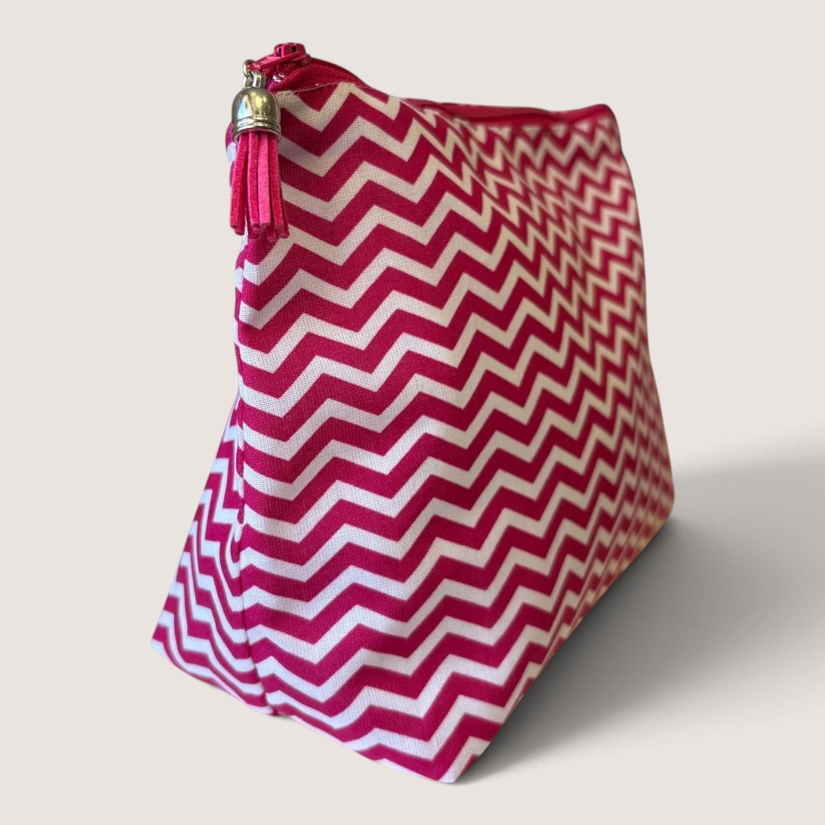 Raspberry Chevron wash bag angled to show the pink and white chevron print, pink zip and bright pink suede tassel with a silver cap