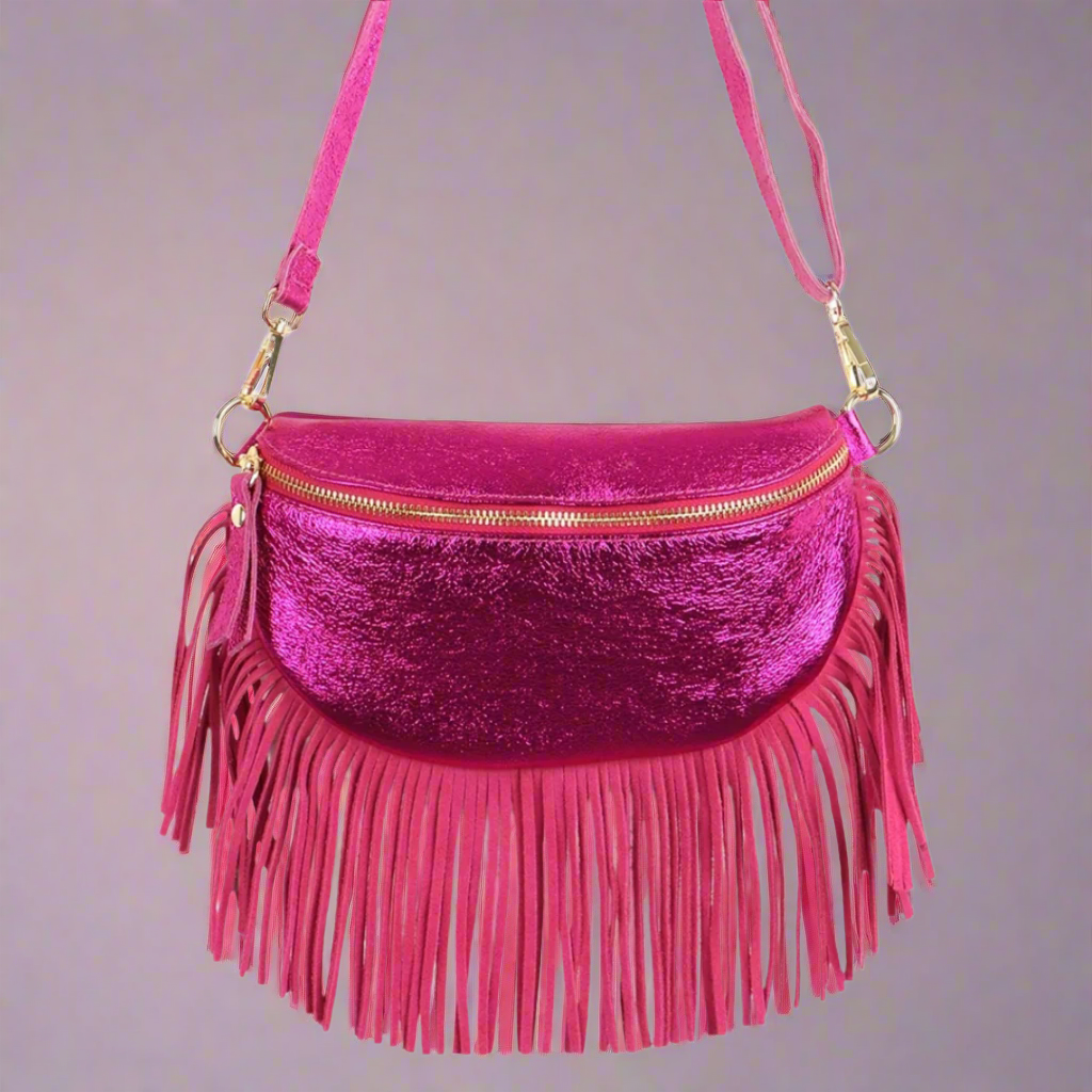 A raspberry metallic leather half moon fringed bag with a zipper closure and gold hardware. It has long pink fringe hanging from the sides and a pink leather strap.