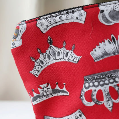 Close-up angled detail of the Red Crowns everyday pouch showing the red fabric printed with silver and grey crowns and the black zip