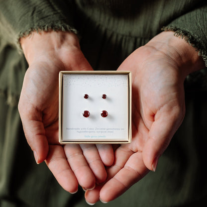 Hands holding a box with red gemstone earrings.