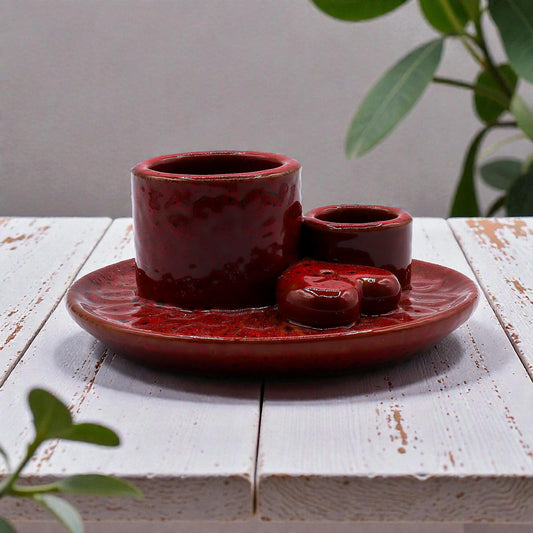 Red ceramic incense and smudge stick burner on a white wooden surface with green leaves in the background